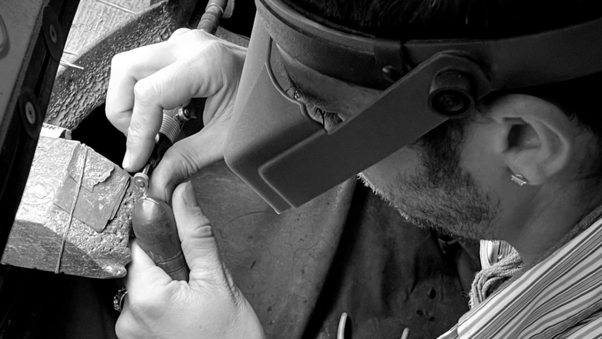 Jeweller working on a ring by hand at the bench, wearing a magnifying visor